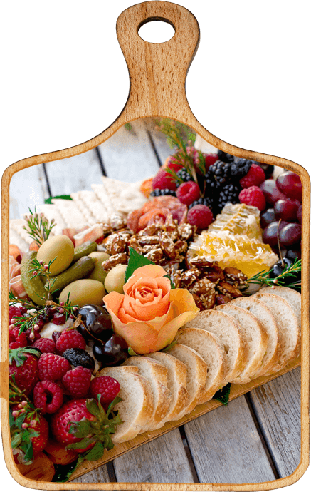 Une photo d’une planche à découper avec du pain, des fruits et des fleurs très colorées. Le tout est placé avec une belle présentation. 
