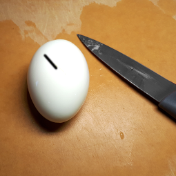 Photo d’un œuf dur et d’un couteau.  Il y a une ligne noire sur l’œuf partant presque du centre et allant au bord sur la gauche. 