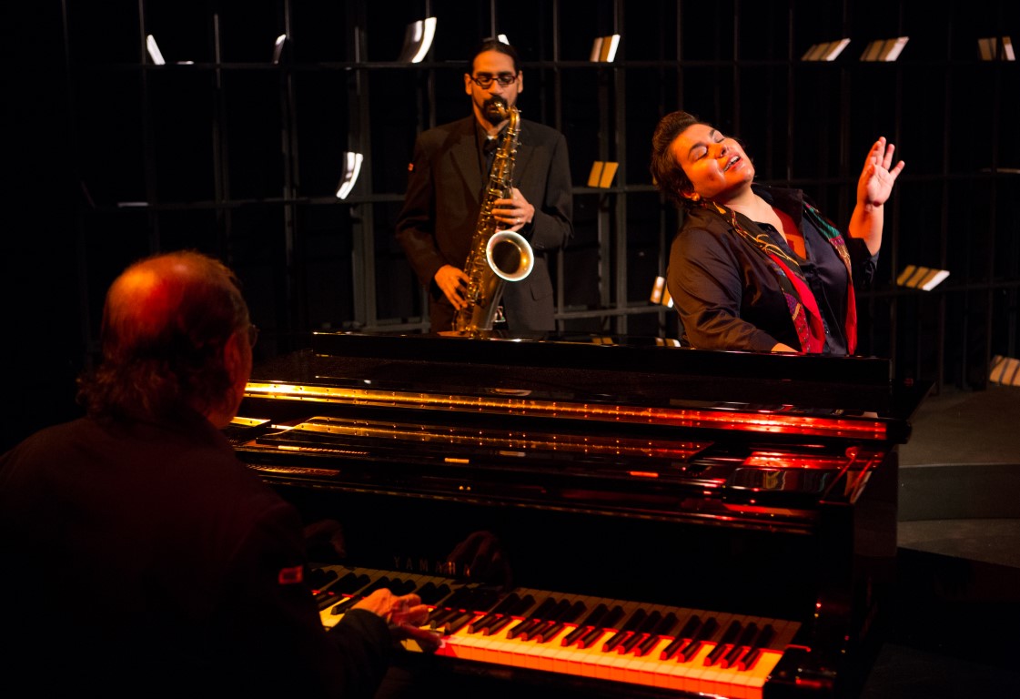 Photo d’une pièce de théâtre où l'on peut voir un pianiste et un joueur saxophone. 