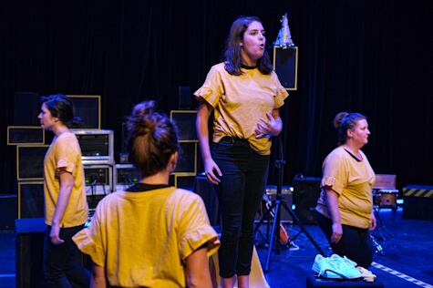 Photo d’une scène de pièce de théâtre avec des gens portant des chandails jaunes. 