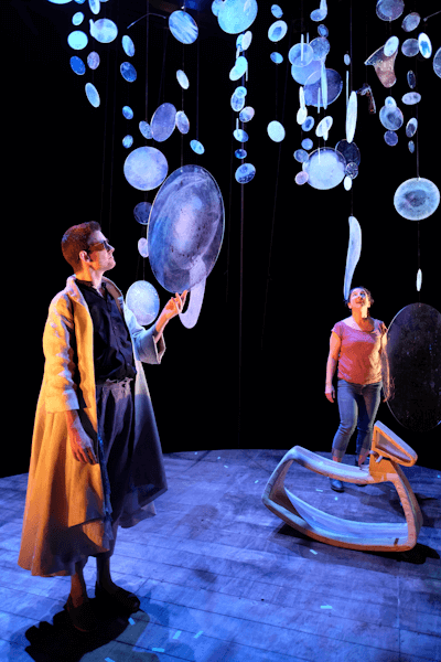 Photo d’une scène de théâtre dont le décor comporte de grosses bulles, et un cheval à bascule. 