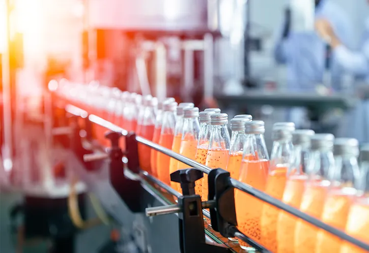 Photo de bouteilles remplies d’un liquide orange avançant sur un tapis roulant dans une usine.