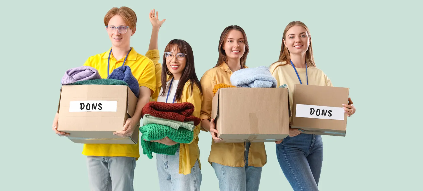 Quatre adolescents, trois filles et un garçon qui tiennent des boîtes de carton remplies de vêtements d’occasions. Le mot dons est écrit sur deux des boîtes.
