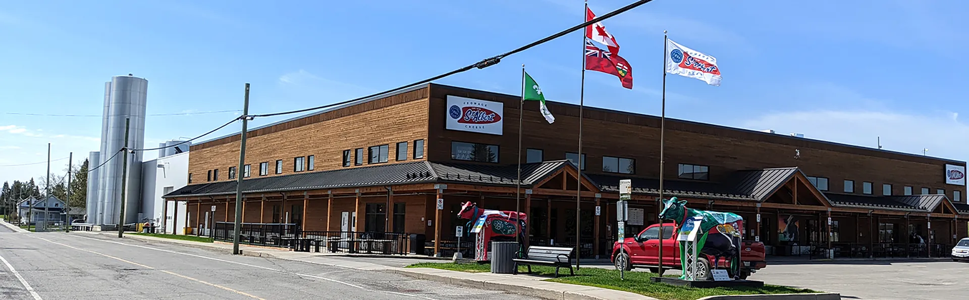 La Fromagerie St‑Albert se dresse sous un ciel clair, avec ses drapeaux flottants et ses sculptures de vaches colorées à l’entrée.