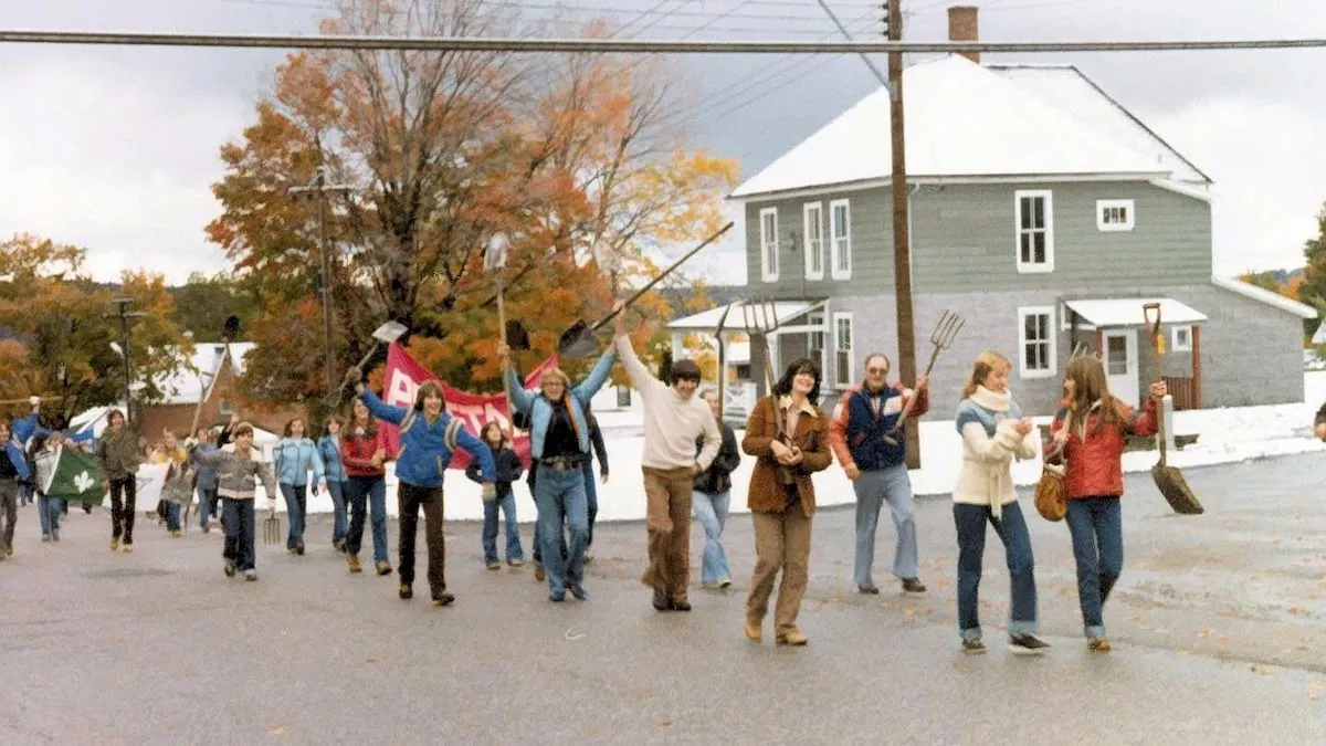Photo couleur montrant des jeunes marchant dans la rue en brandissant des pelles et des fourches de façon festive.