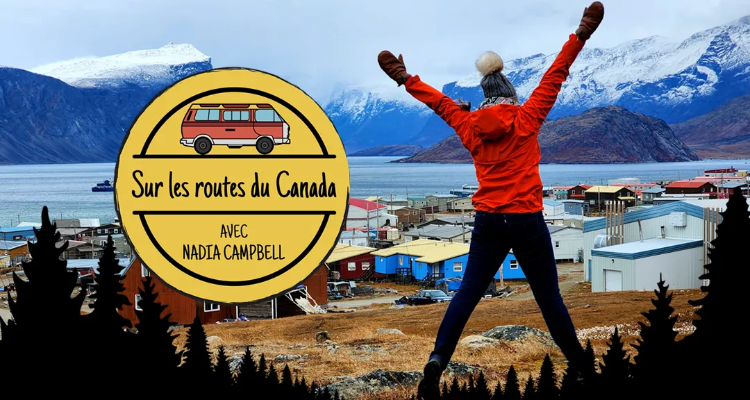 Photo de Nadia Campbell se tenant, les bras levés, devant un paysage de montagnes enneigé et d’un petit village près de l’eau.