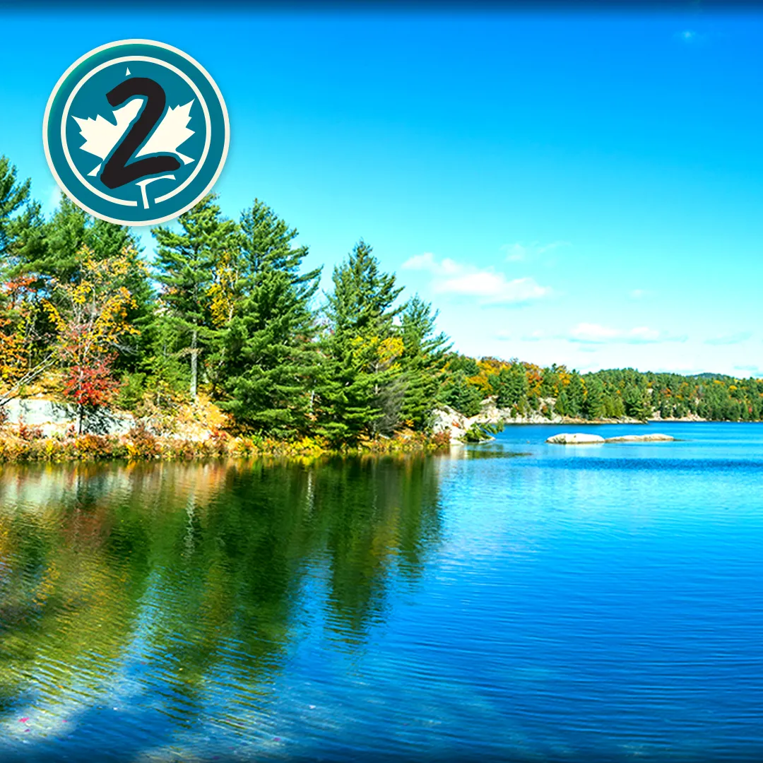 Photo d’un lac en automne sous un ciel bleu. Cercle contenant le chiffre 2 et une feuille d’érable.