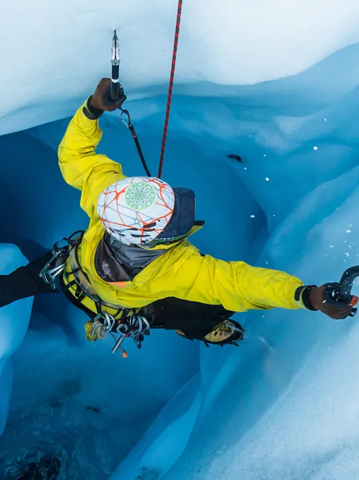 Photo d’une personne qui pratique l’escalade de glace. Elle s’accroche à une paroi glacée grâce à une corde de sécurité, des crampons et des piolets.