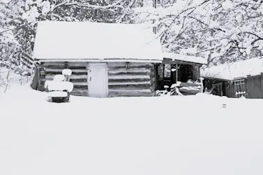 Cabane en bois recouverte de neige au cœur d’un paysage hivernal, entourée d’arbres givrés.
