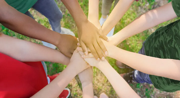 Vue en plongée sur des mains de cinq enfants qui forment un cercle. Leurs mains sont posées les unes par-dessus les autres au centre du cercle.