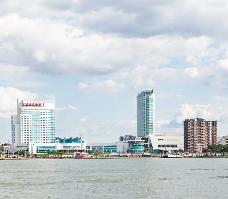 Paysage urbain de Windsor, vue de la rivière. Une foire avec des manèges prend vie au bord de l’eau. Plusieurs bâtiments dont ceux du Colisée Ceasars habitent l’espace en arrière-plan.