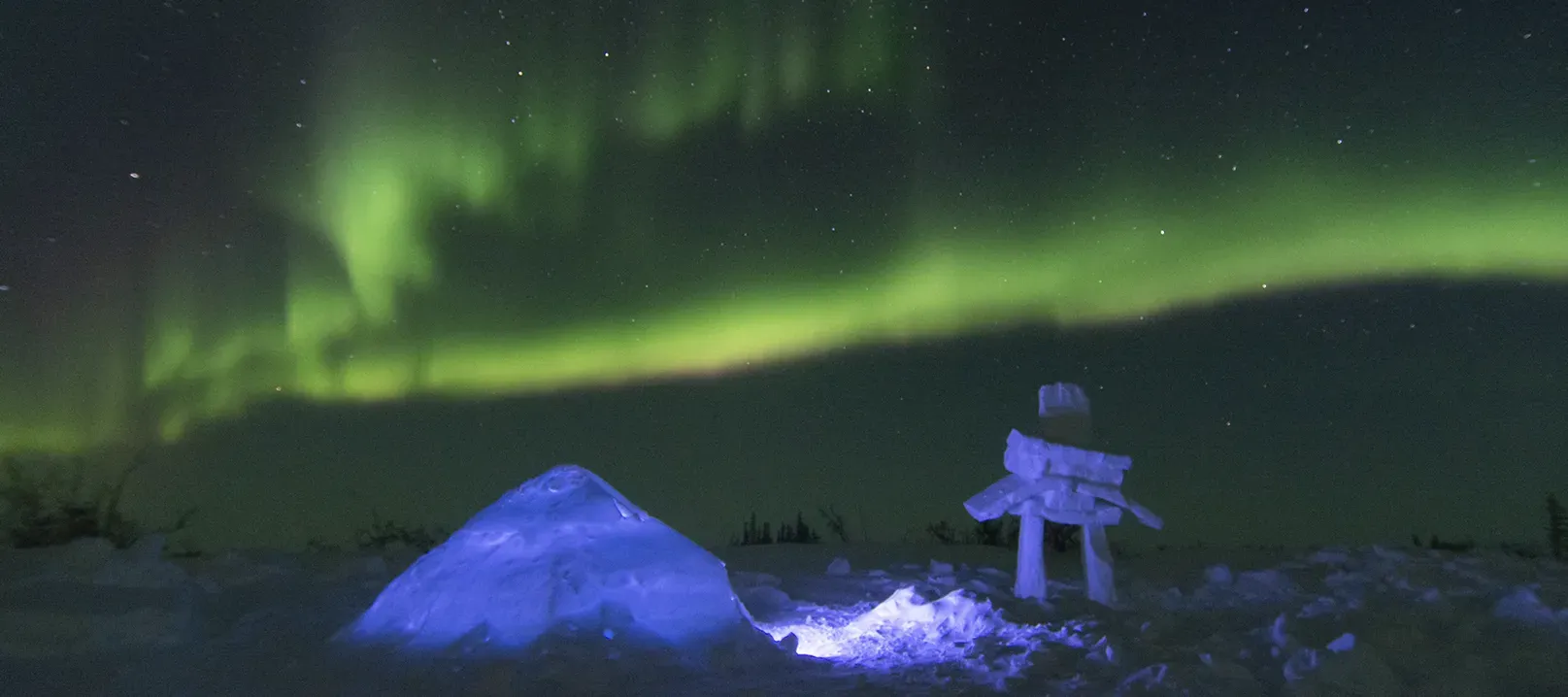 Photo d’un igloo et d’un inukshuk sous une aurore boréale.