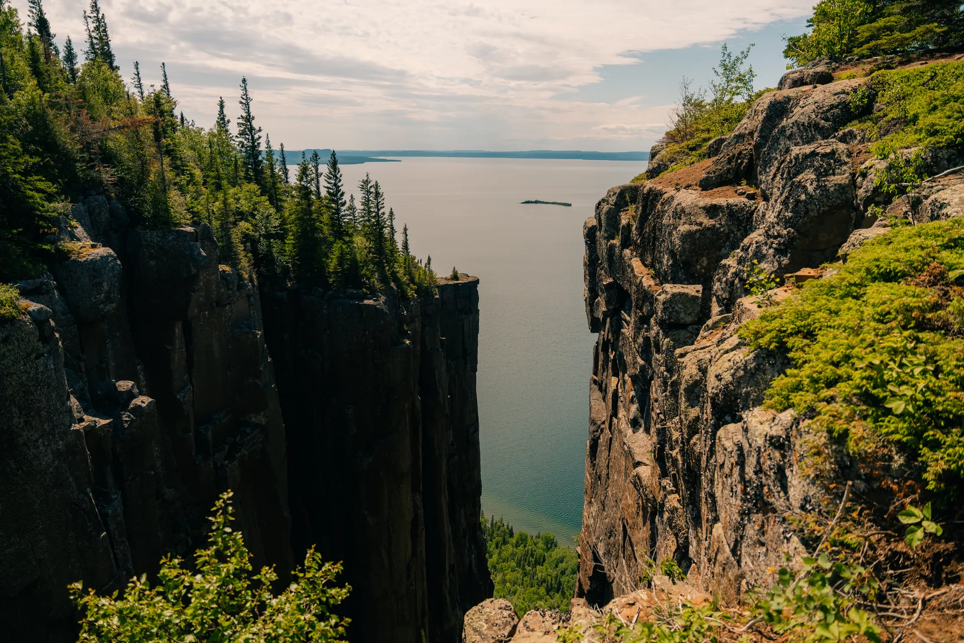 Canyon entre deux falaises escarpées avec des arbres au sommet des rochers en avant plan d’un lac calme. Photo prise sous un ciel partiellement nuageux.