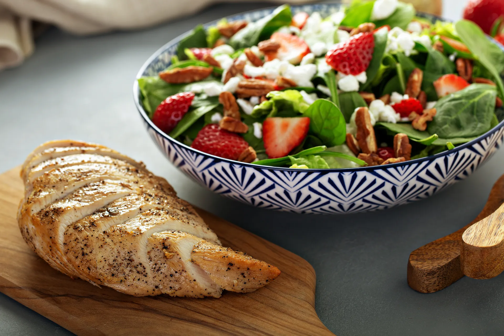 Une poitrine de poulet coupée en tranches à côté d’un bol rempli d’épinards, de fraises, de noix et de fromage de chèvre.