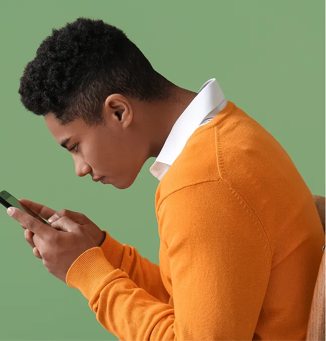Un adolescent consulte son cellulaire. Il est assis et il est légèrement penché vers l’avant.