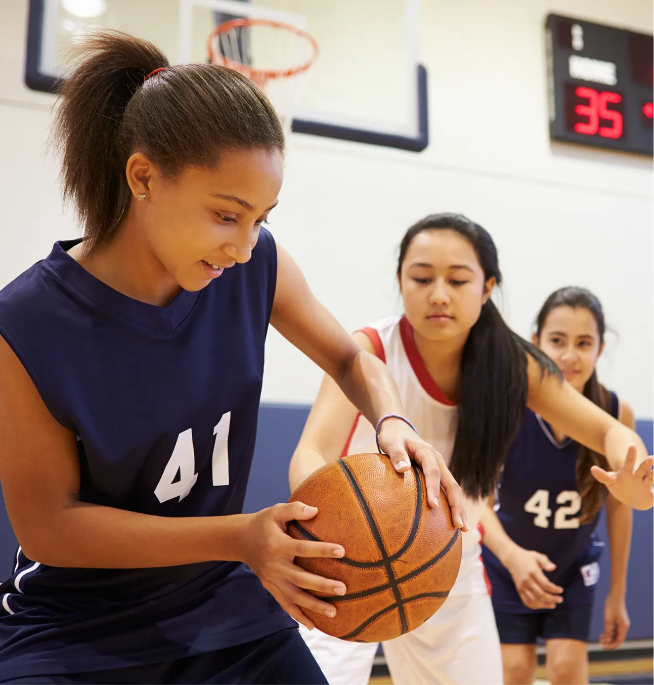 Une fille tient un ballon de basketball dans ses mains. Une autre fille tente de le lui prendre.
