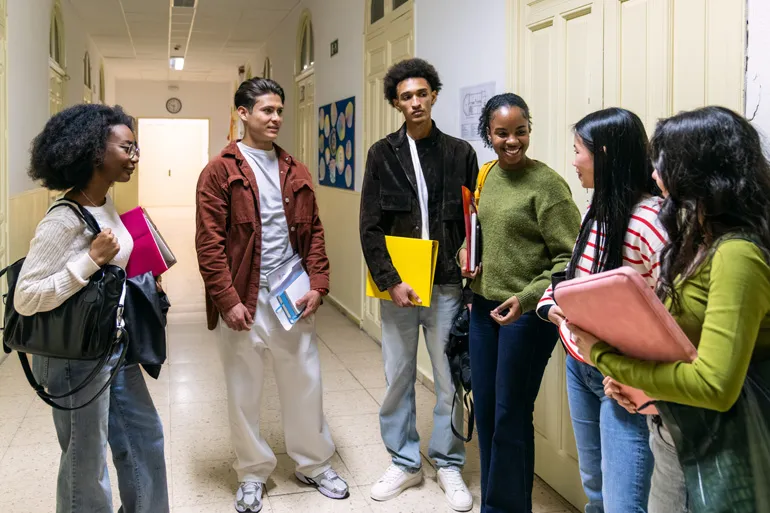 Un groupe de six adolescents, garçons et filles, discutent et sourient joyeusement dans un couloir d’école.