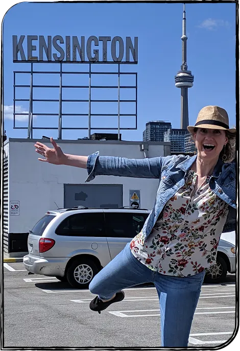 Photo de Nadia Campbell se tenant debout sur une jambe avec les bras à l’horizontale dans un stationnement. Derrière elle, sur un bâtiment, une enseigne indique : « KENSINGTON ».