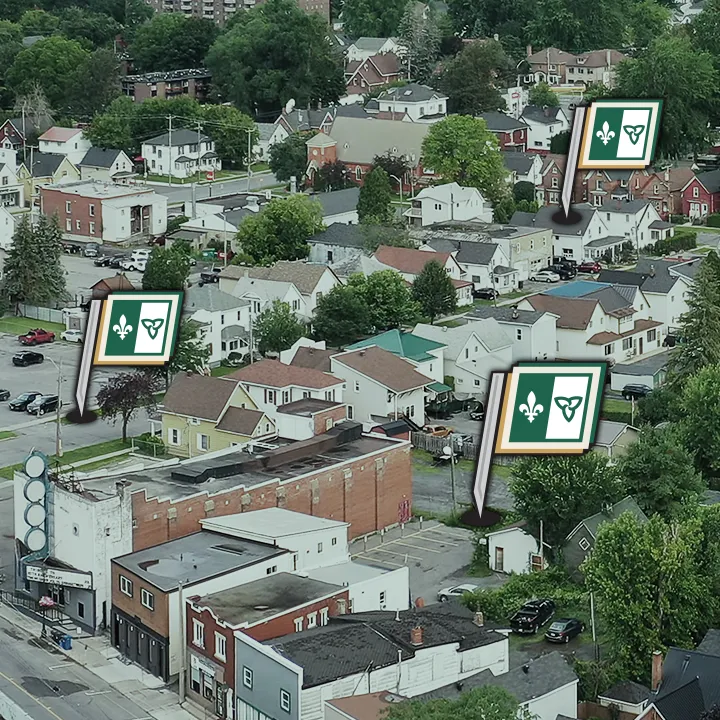 Vue aérienne d’une ville ontarienne. Quatre drapeaux franco-ontariens s’élèvent soudainement de quatre différents bâtiments.