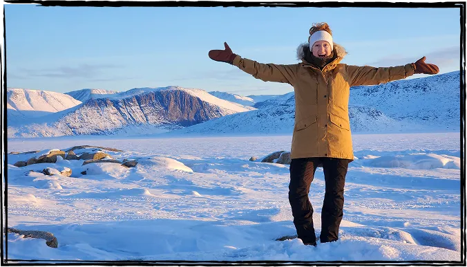 Photo de Nadia Campbell souriante, les bras levés, debout au milieu d’un paysage hivernal.
