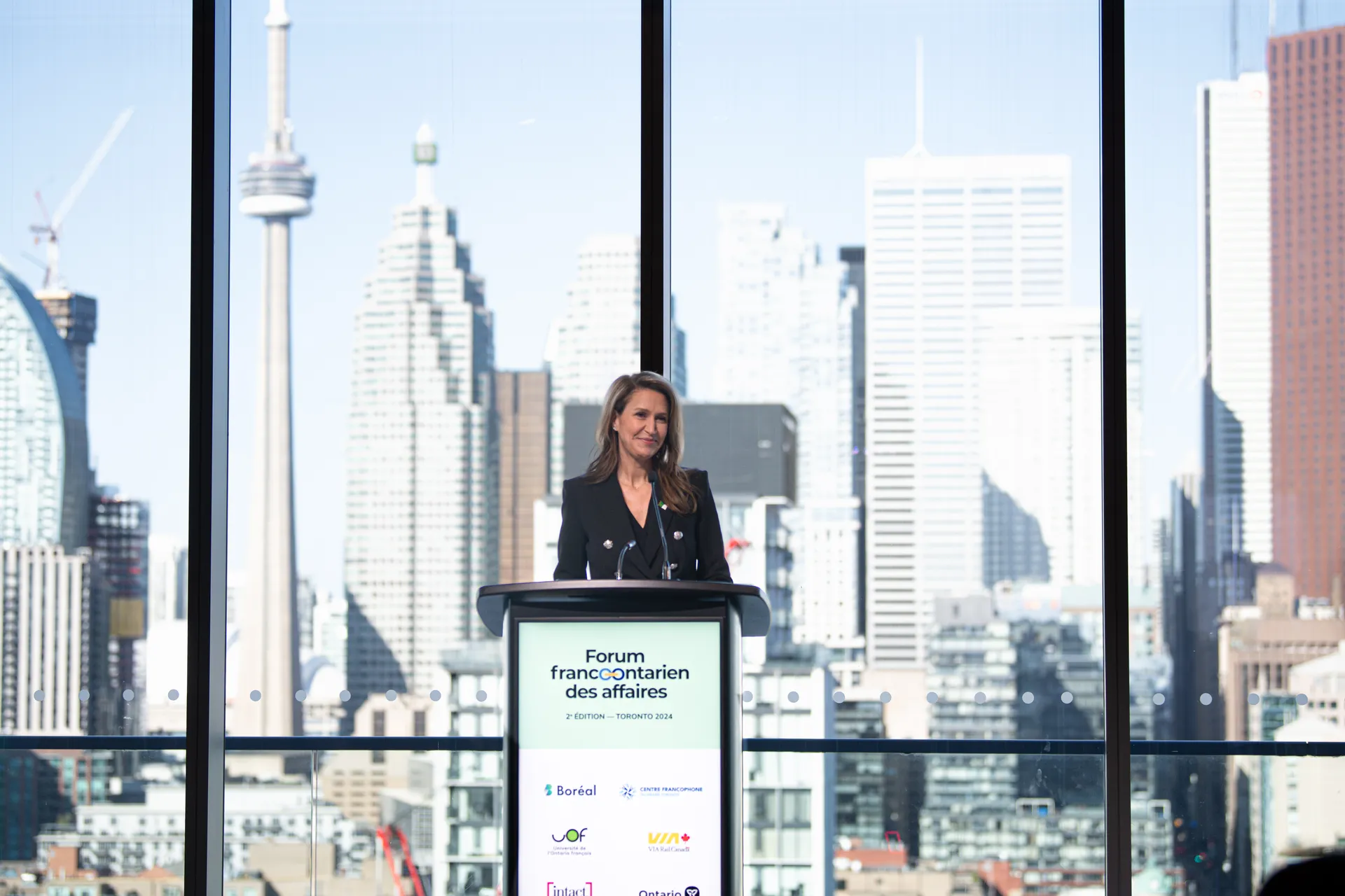 Madame Caroline Mulroney prend la parole au Forum franco-ontarien des affaires, devant la skyline de Toronto, pour promouvoir la collaboration et l’entrepreneuriat francophone.